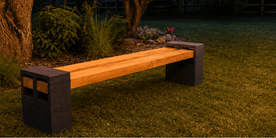 Cinder block garden bench ideas showing a simple DIY outdoor bench made with black cinder blocks and wooden planks under warm string lights in a cozy backyard garden.