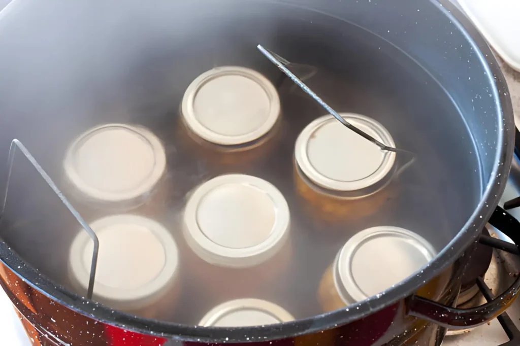 Mason jars processing in a steaming water-bath canner with a metal jar rack on a stovetop.