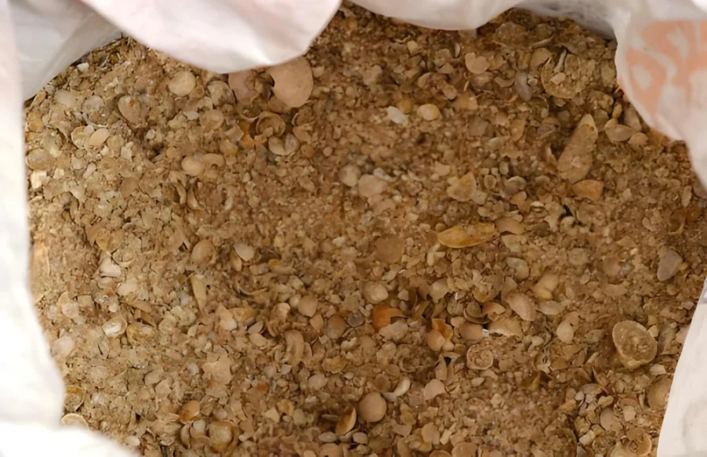 Close-up of coarse bone meal in a bag, showing one of the phosphorus-rich organic fertilizer types used in garden soil.